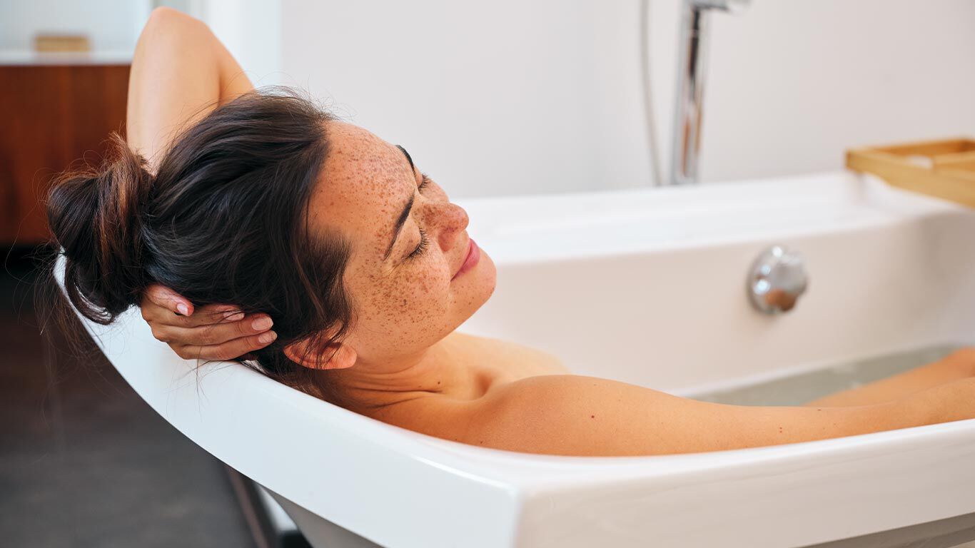 Een vrouw met bruin haar in een knot, ontspannen liggend in het bad.